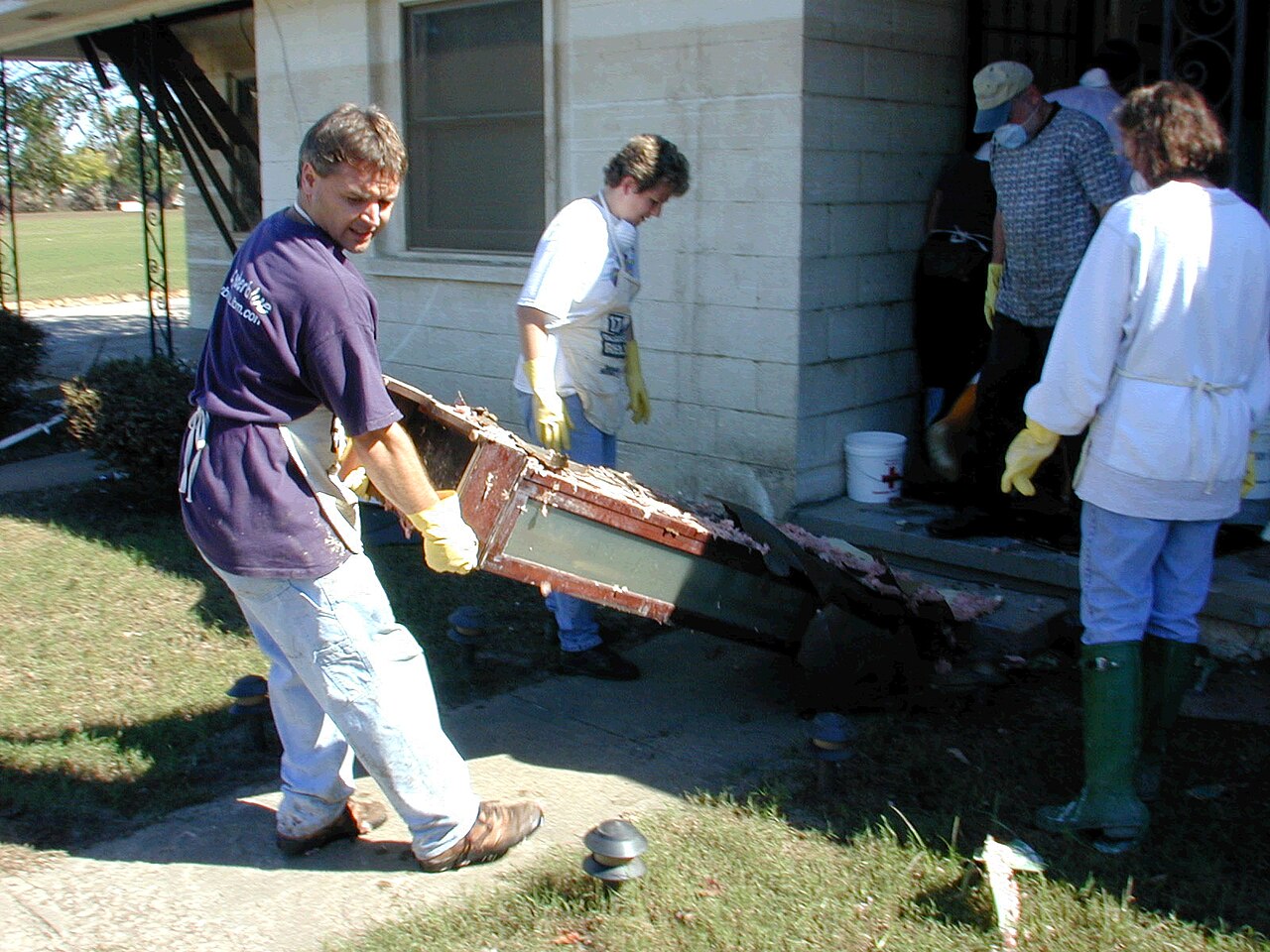 A cleanup crew in gloves and boots carries water-damaged furniture and materials out of a flooded home.
